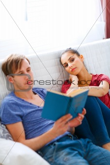 Girl boring while her boyfriend reading book
