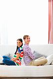 Cheerful young couple sitting on sofa back to back
