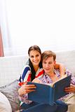 Happy young couple sitting on couch and looking photo album 
