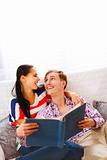 Laughing young couple sitting on couch and looking in photo album 
