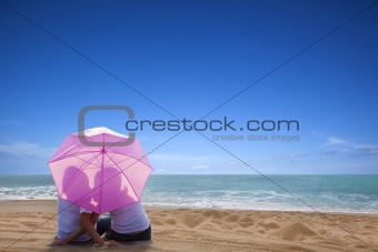 young couple romantic kissing at the beach with the umbrella