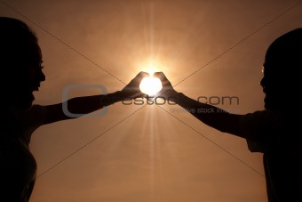 happy young couple making heart shape with hands  at sunset