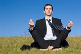 Meditating young businessman on the meadow