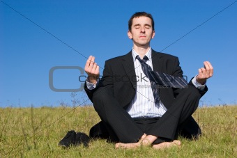Meditating young businessman on the meadow