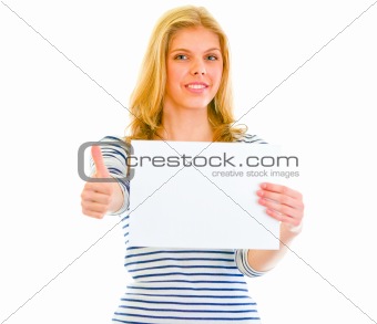 Smiling teen girl holding blank paper and showing thumbs up

