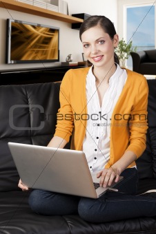 girl on sofa with laptop, she smiles and looks in to the lens