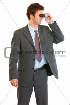 Modern businessman looking through binoculars in corner
