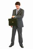 Full length portrait of modern businessman with suitcase looking on watch
