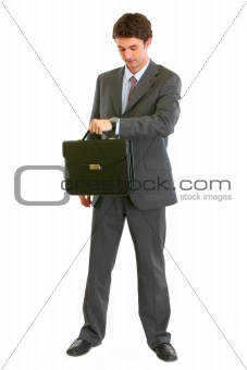 Full length portrait of modern businessman with suitcase looking on watch

