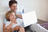 Father and child using laptop in bed