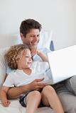 Smiling father and child on bed with laptop