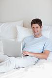 Smiling man lying in bed with notebook