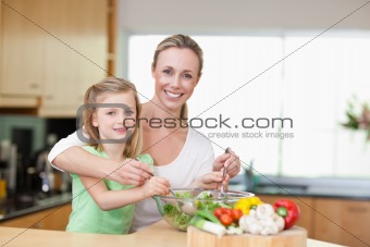 Smiling mother and daughter stirring salad