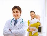 Portrait of pediatrician doctor and mother with baby in background

