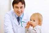 Portrait of interested baby with stethoscope and pediatric doctor in background
