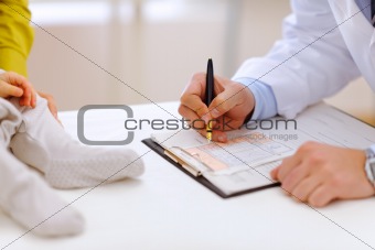 Closeup on doctor's hands writing in clipboard and baby's legs
