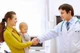 Mother holding baby and handshaking pediatric doctor's hand 
