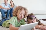 Young children using a tablet computer while their happy parents are watching