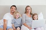Family sitting on the bed with laptop