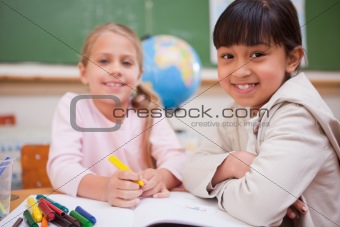 Smiling schoolgirls drawing while looking at the camera