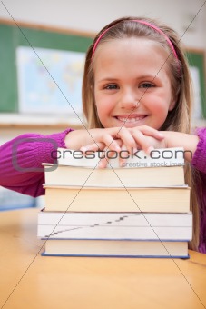 Portrait of a happy schoolgirl posing with a stack of books