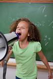 Portrait of a cute schoolgirl screaming through a megaphone