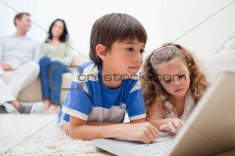 Kids using laptop on the carpet with parents behind them
