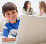 Boy using laptop on the carpet with his family behind him