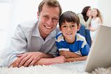Smiling son and dad using laptop on the carpet