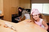 Girl sitting in the kitchen while her mother puts cookies into the oven