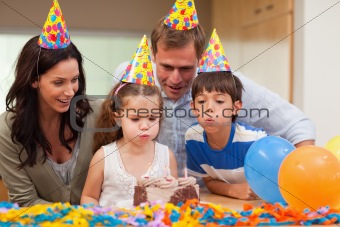 Boy helping his little sister to blow out the candles on her birthday cake