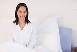 Smiling woman in pajamas sitting on her bed