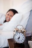 Alarm clock ringing next to woman in bed