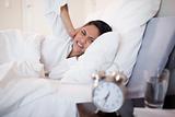 Woman covering her ears cause of ringing alarm clock