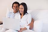 Couple using their laptop while sitting on the bed