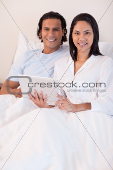 Couple using tablet pc in their bed