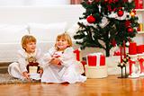 Two happy twins girl sitting with gift boxes near Christmas tree