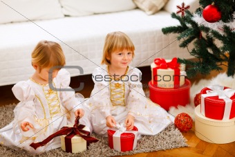 Two cute twins girls opening presents near Christmas tree