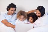 Family sitting on the bed surfing the internet
