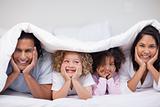 Smiling family hiding under the blanket