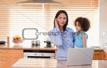 Mother and daughter with cellphone and laptop in the kitchen together