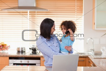 Mother and daughter using notebook and cellphone in the kitchen together