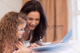 Side view of mother and daughter reading a book together