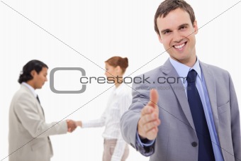 Businessman extending hand with hand shaking colleagues behind him
