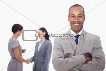 Smiling businessman with folded arms and colleagues behind him