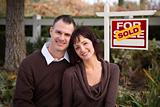 Happy Attractive Caucasian Couple in Front of Sold Real Estate Sign.