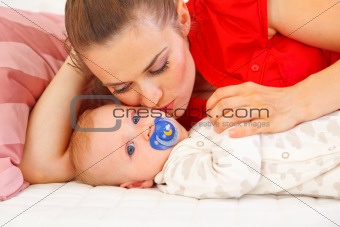 Young mother laying on couch and kissing baby