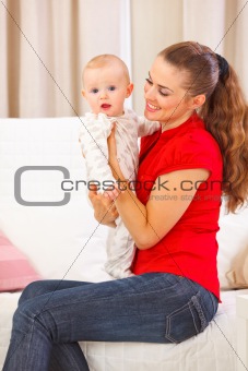 Baby playing with mother on divan