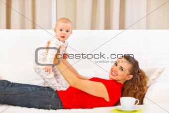 Smiling mother and adorable baby playing on couch