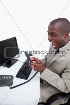 Portrait of an angry businessman answering the phone while using a monitor